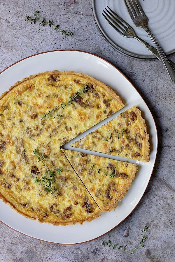 Photo of Caramelized Onion and Goat Cheese Tart on white serving platter with two pieces cut.