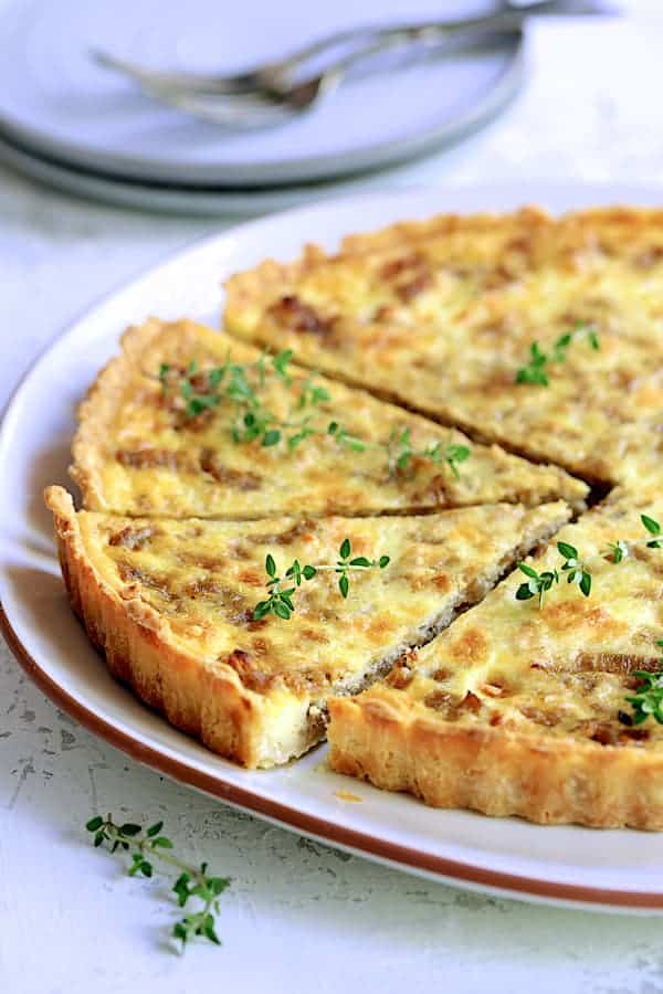 Close-up photo of Caramelized Onion and Goat Cheese Tart on white serving platter with two pieces cut.