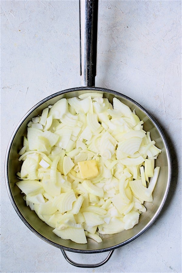 Photo of raw onions in stainless steel pan with butter in the middle.