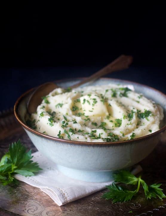 Celery root puree in bowl garnished with fresh chopped parsley.