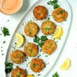 Nine shrimp cakes on oval white platter garnished with lemon and parsley.