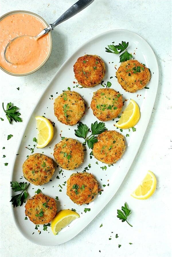 Nine shrimp cakes on oval white platter garnished with lemon and parsley.