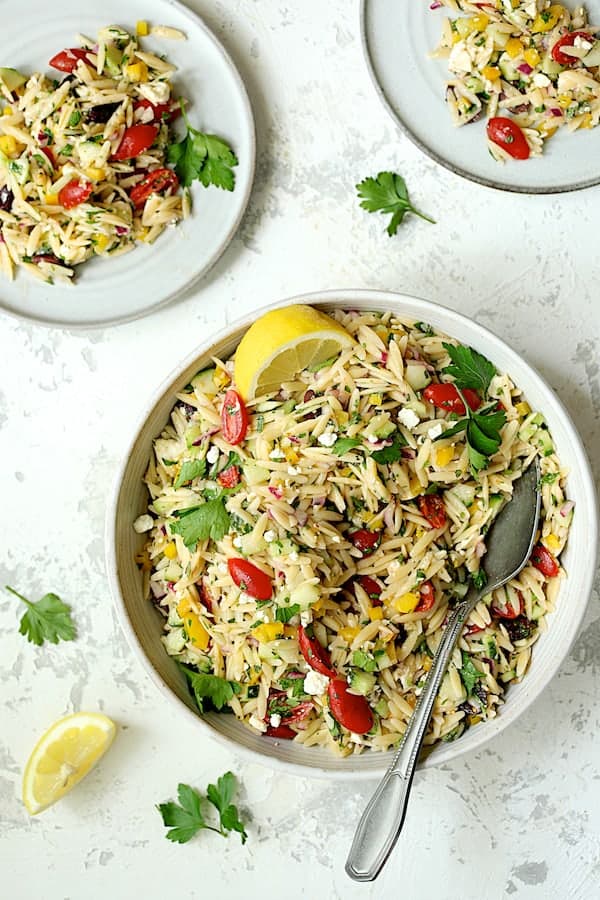 Photo of Greek Orzo Pasta Salad served from white serving bowl onto small white plates.