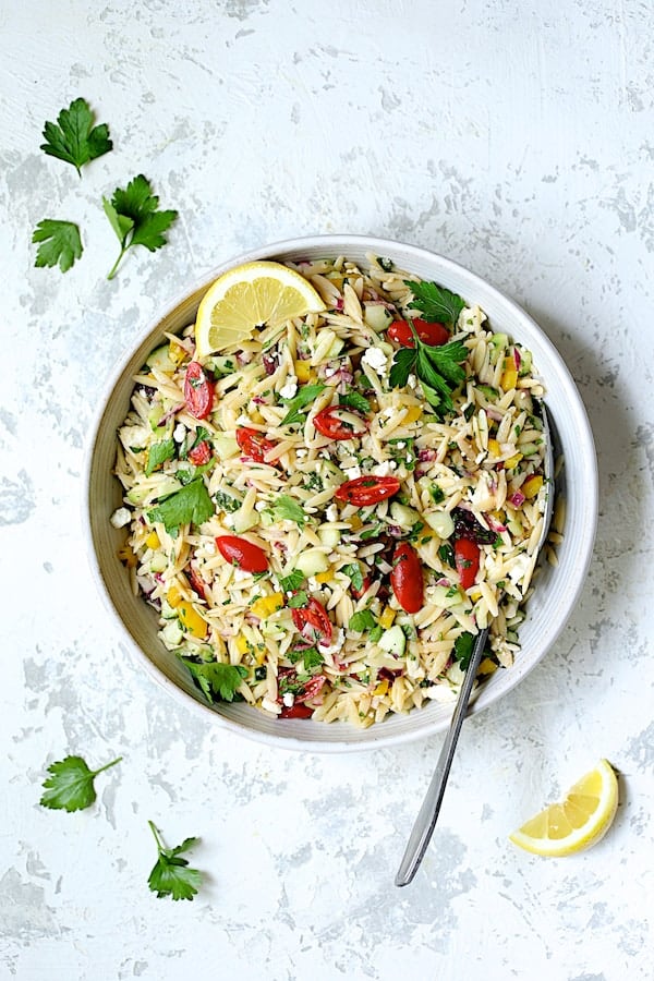 Photo of Greek Orzo Pasta Salad in white serving bowl with serving spoon.