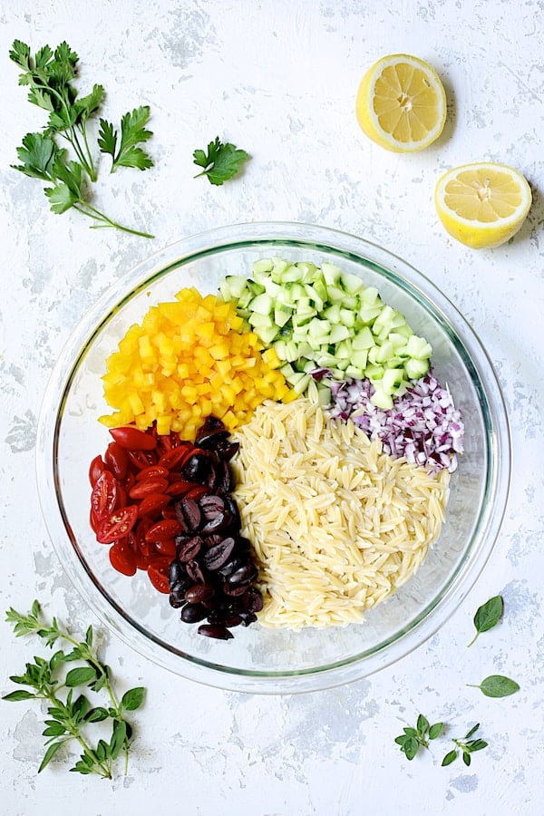 Photo of all the ingredients for Greek Orzo Pasta Salad in glass bowl not combined.