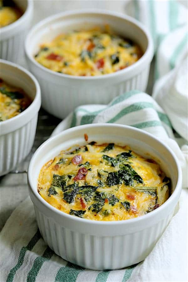Photo of Hash Brown Frittatas with Kale, Bacon and Cheddar on white and green striped towel with three more frittatas in the background.