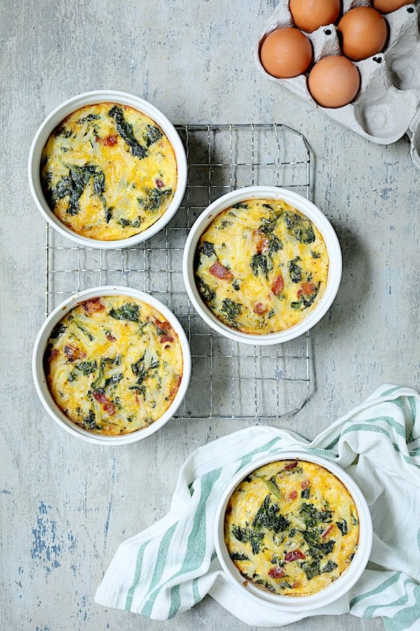 Photo of baked Hash Brown Frittatas with Kale, Bacon and Cheddar with three on cooling rack and one on green striped towel.