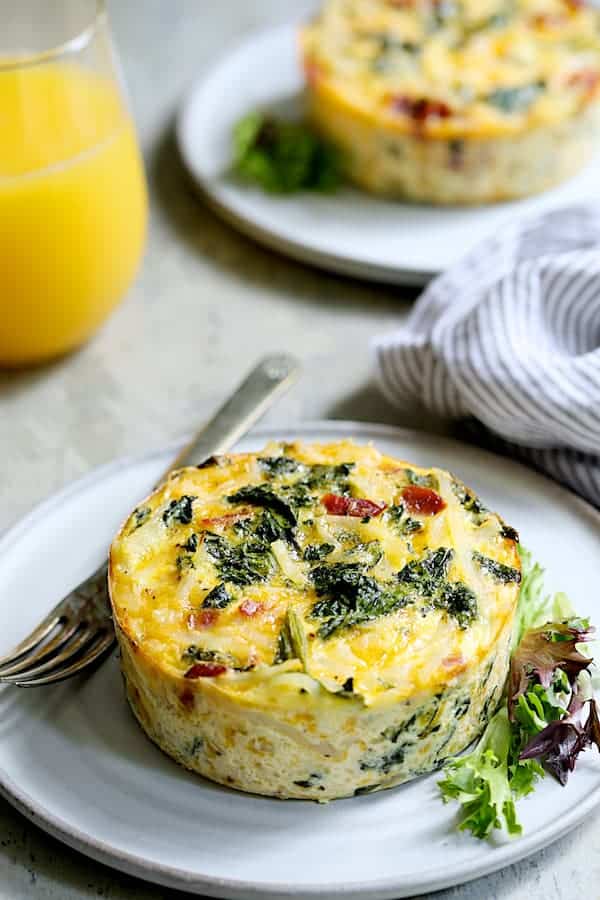 Photo of baked Hash Brown Frittata with Kale Bacon and Cheddar removed from ramekin on plate with fork, garnished with greens.