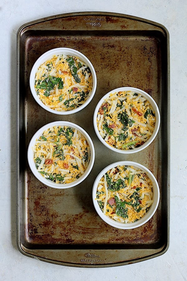 Photo of four Hash Brown Frittata with Kale, Bacon and Cheddar on baking sheet before custard is poured in.