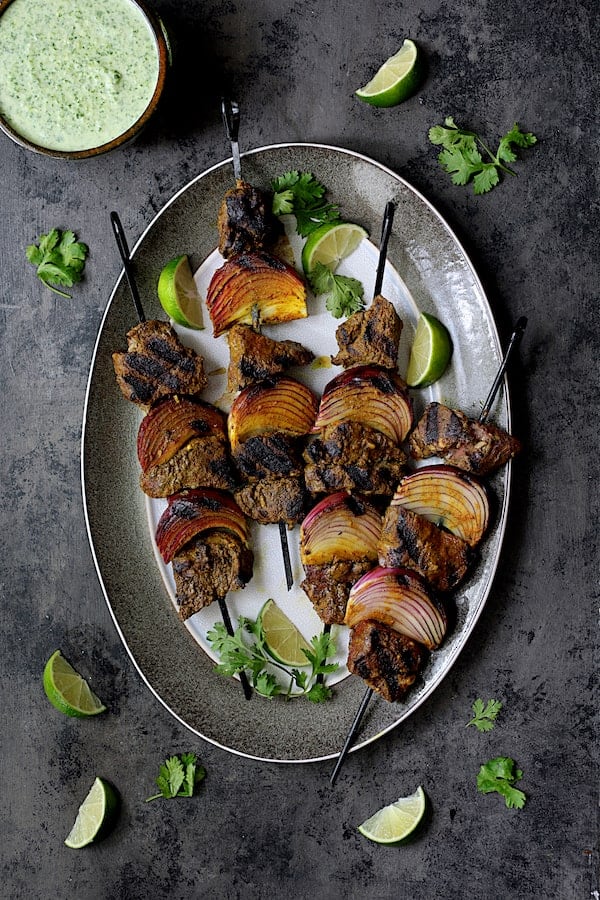 Indian-Style Beef Kabobs with Cilantro-Coconut Sauce - Another overhead shot of kabobs on gray-rimmed platter garnished with cilantro and lime wedges
