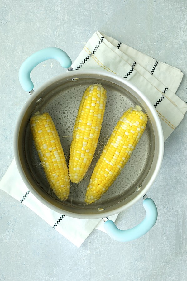 Photo of three cobs of corn after being parboiled in cookware.