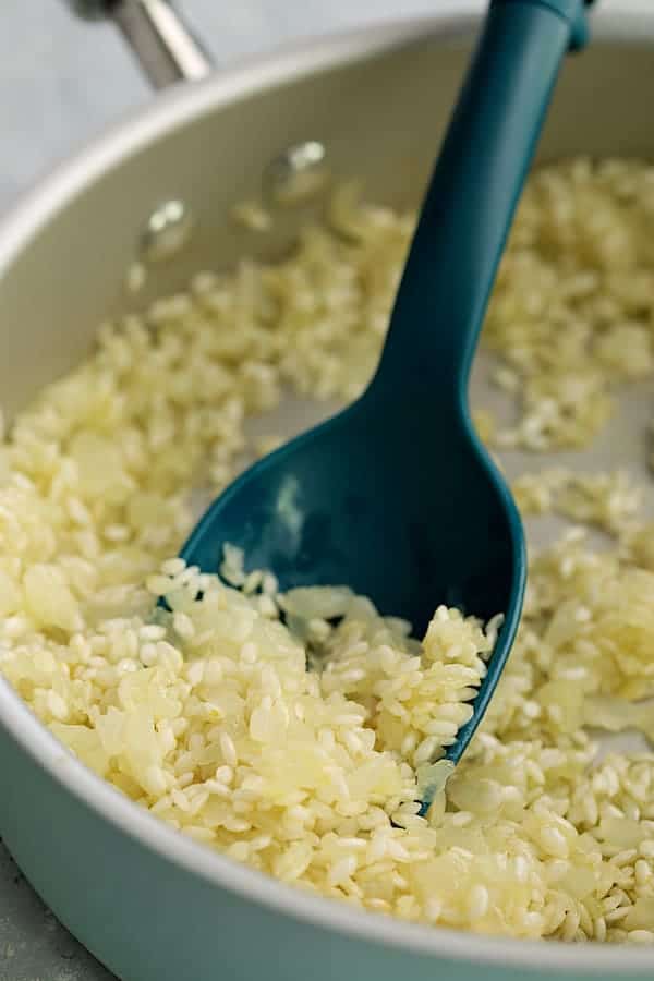 Photo of risotto being stirred with blue spoon.