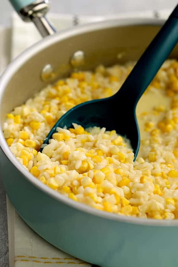 Photo of risotto being stirred with blue spoon after sweet corn is added.