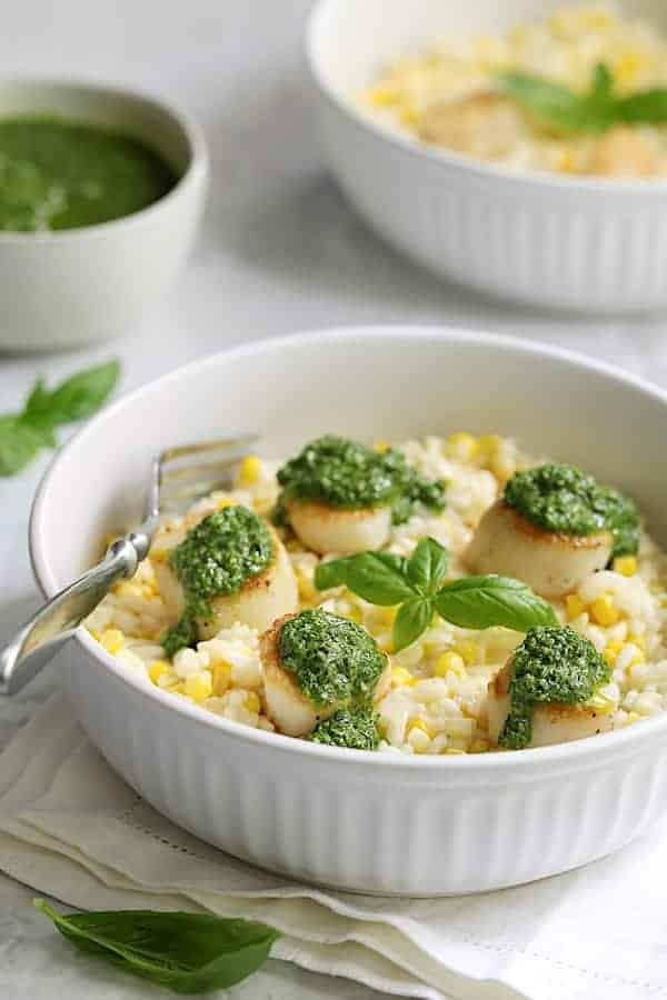 Photo of Sweet Corn Risotto with Seared Sea Scallops and Basil Salsa Verde in white serving bowl garnished with fresh basil.