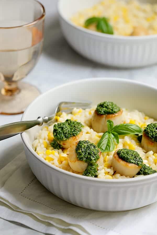 Photo of Sweet Corn Risotto with Seared Sea Scallops and Basil Salsa Verde in white bowl garnished with fresh basil.