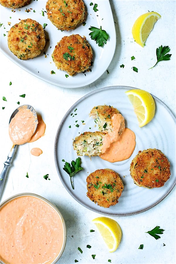 Photo of Shrimp Cakes with Roasted Red Bell Pepper Mayonnaise on plates with one cut in half and garnished with lemon wedges and parsley.