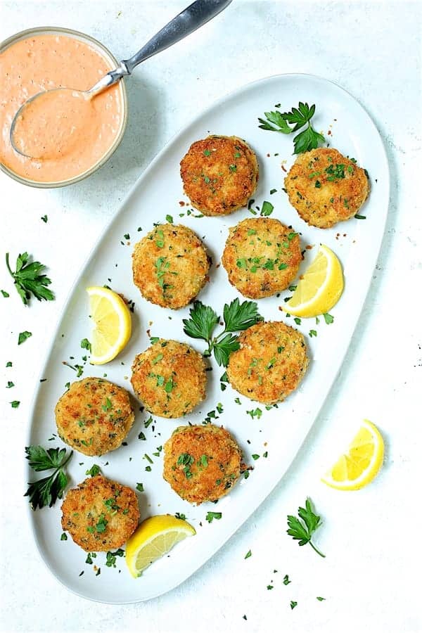 Photo of Shrimp Cakes with Roasted Red Bell Pepper Mayonnaise on white oval platter garnished with lemon and parsley.