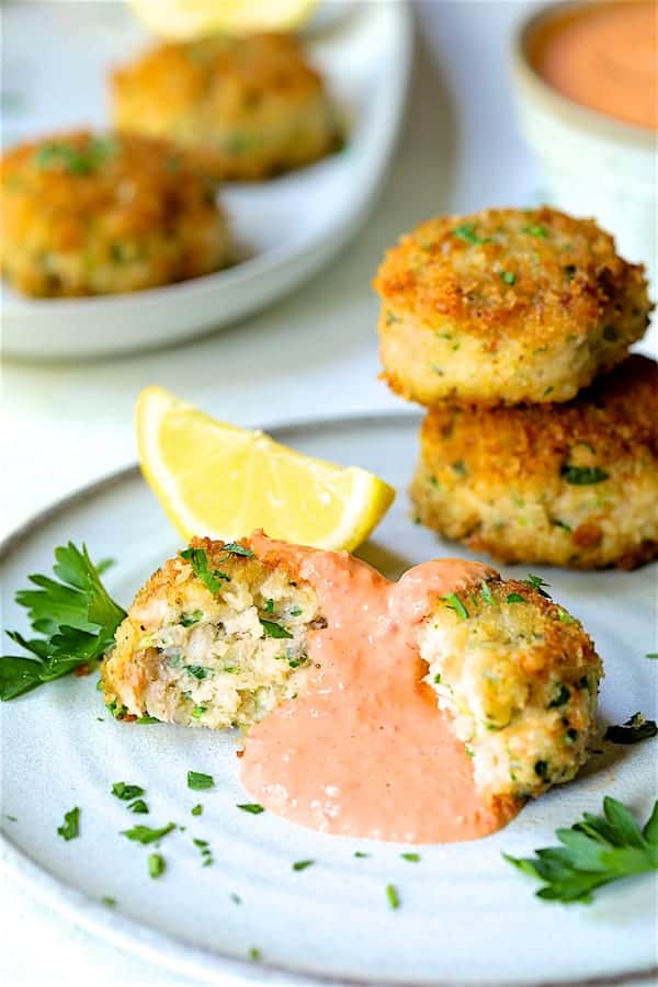 Close-up photo of a serving of Shrimp Cakes with Roasted Red Bell Pepper Mayonnaise on plate garnished with lemon wedge and parsley.