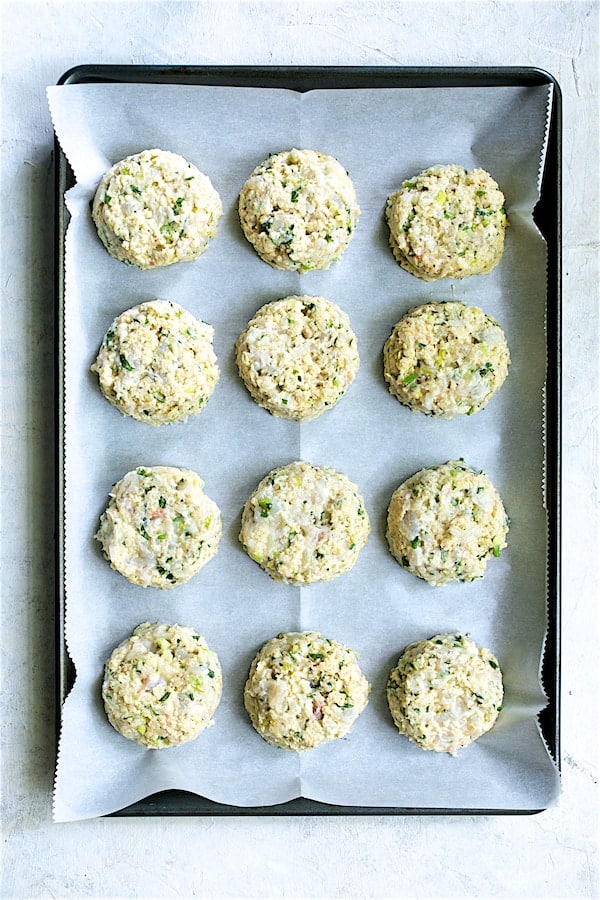 Photo of uncooked assembled shrimp cakes on parchment paper-lined baking sheet.