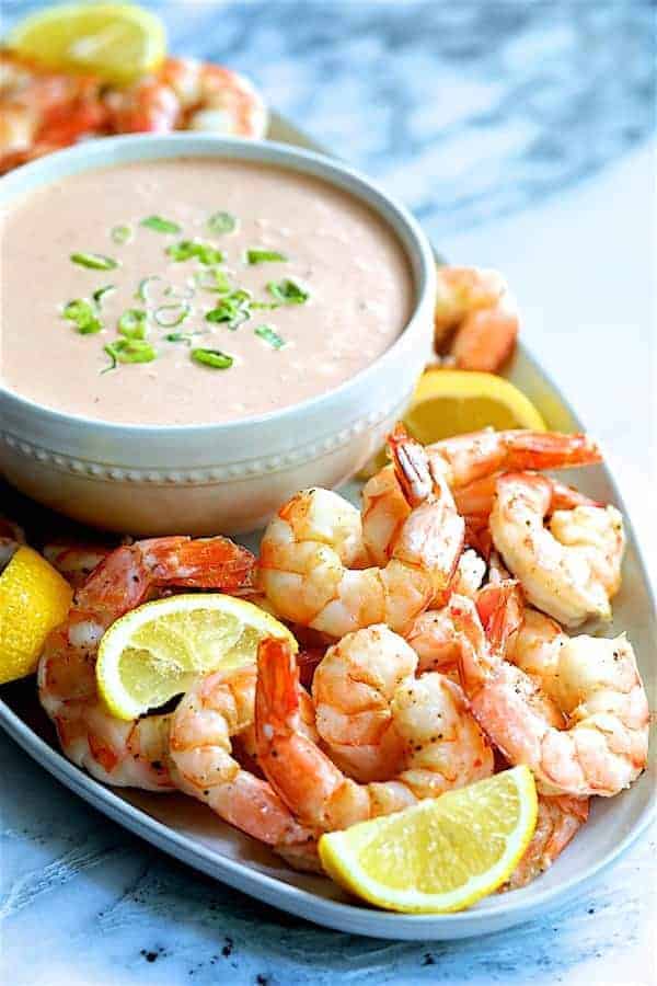 Close-up photo of Shrimp Cocktail Louis on white platter with sauce garnished with lemon wedges.