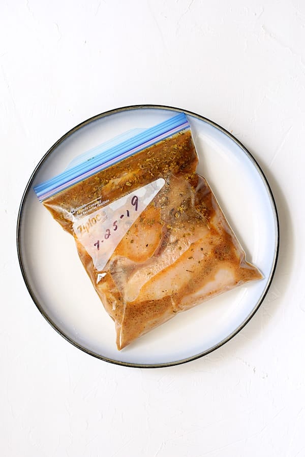 Photo of chicken in marinade in zipper-top bag on plate.