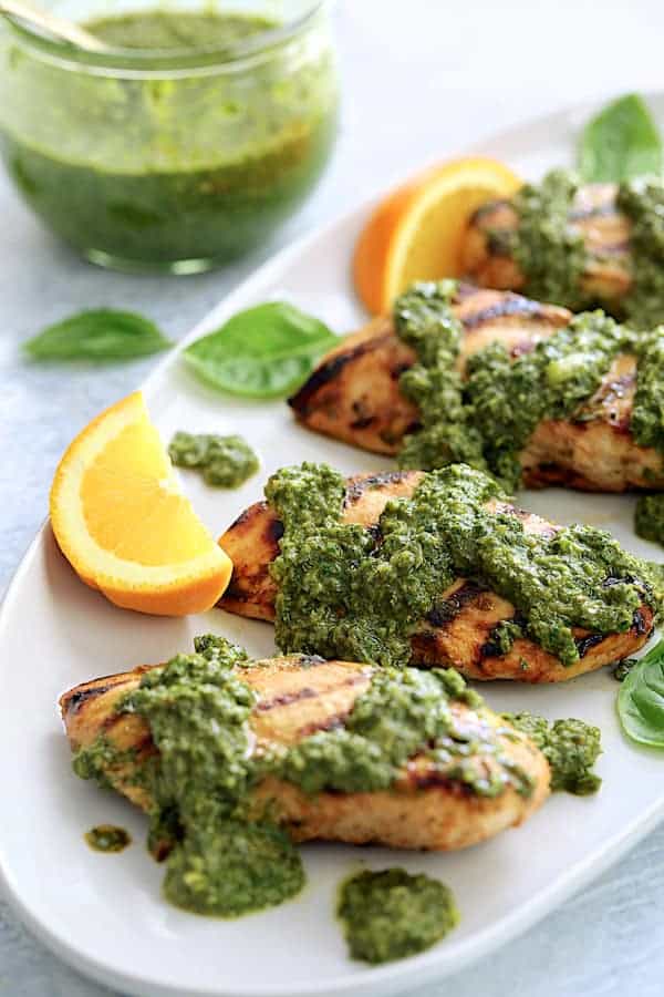 Close-up photo of Grilled Citrus Chicken with Spicy Basil Chimichurri Sauce on white serving platter garnished with orange wedges.