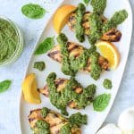 Four chicken breasts with basil chimichurri on oval white platter.