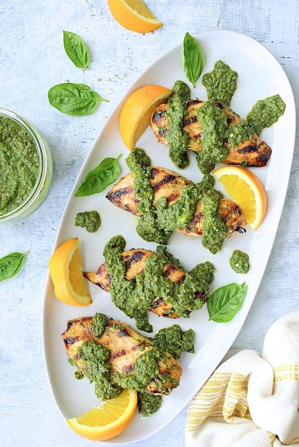 Four chicken breasts with basil chimichurri on oval white platter.