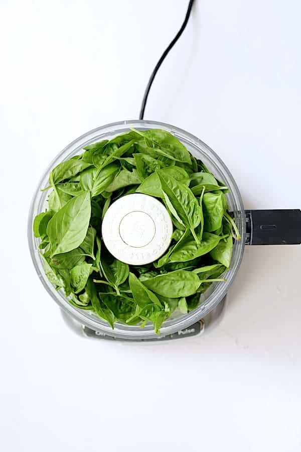 Photo of fresh basil leaves in food processor.