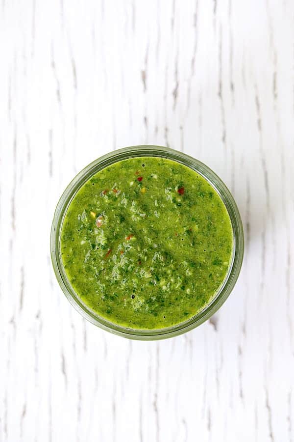 Photo of Purslane Chimichurri in glass jar on white background.