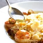 Seared Sea Scallops with Jalapeno Brown Butter in white bowl with spoon drizzling butter over a scallop.
