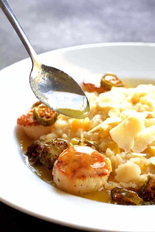 Seared Sea Scallops with Jalapeno Brown Butter in white bowl with spoon drizzling butter over a scallop.