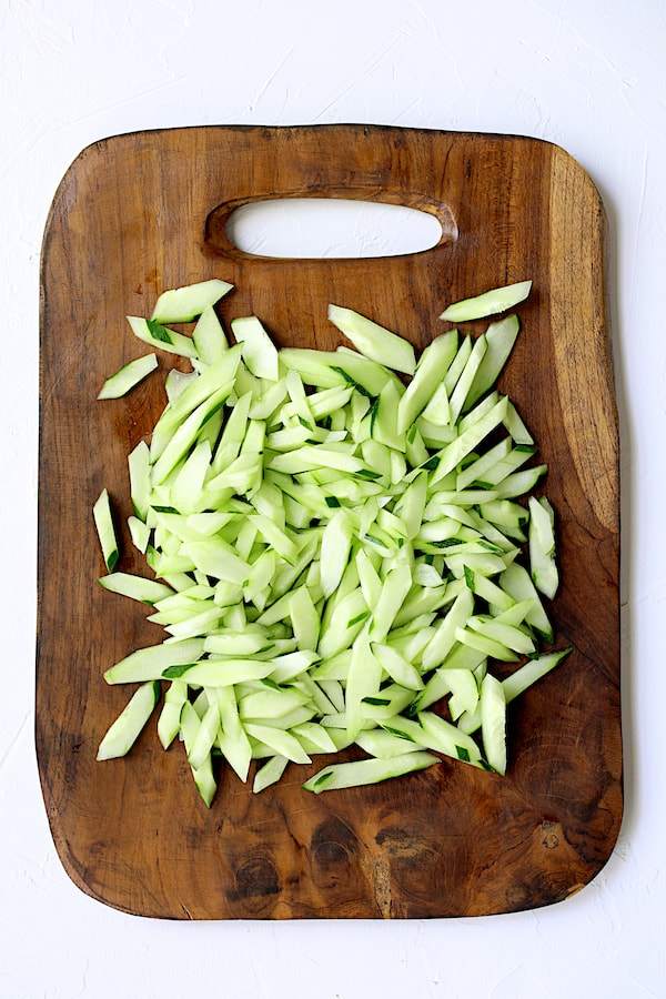 Photo of sliced cucumber on rustic wood cutting board.