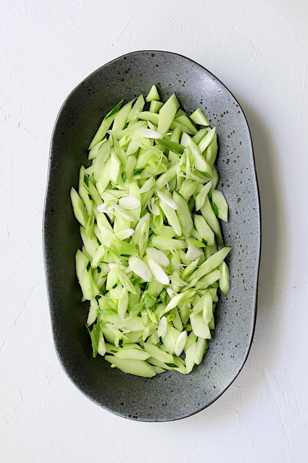 Photo of sliced cucumber and scallion on black platter.