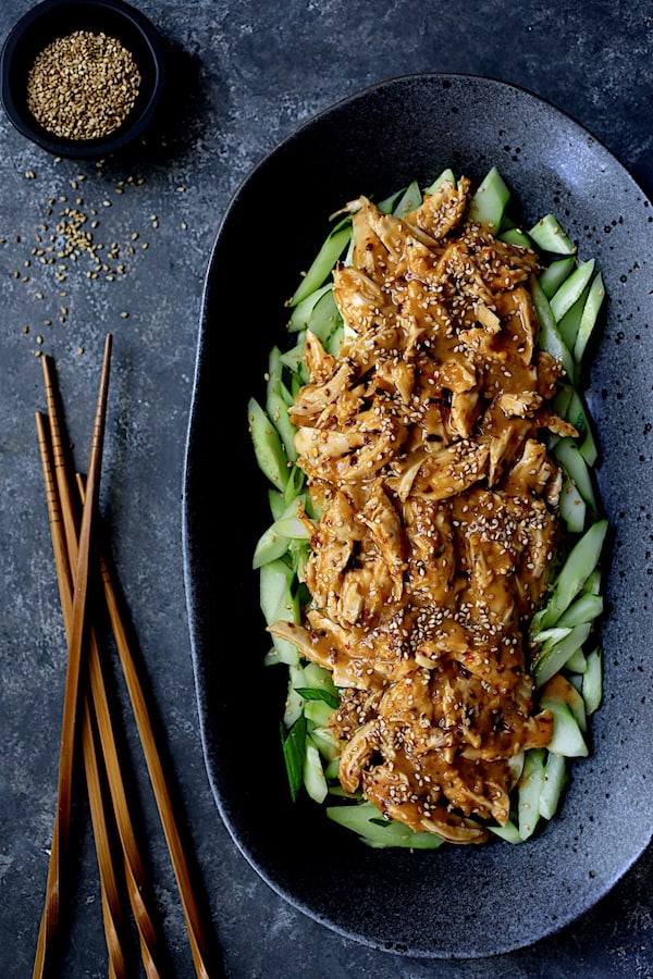 Photo of Sichuan Bang Bang Chicken on black oval platter with chopsticks and garnished with sesame seeds.