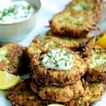 Zucchini Ricotta Fritters with yogurt chive topping garnished with lemon slices.