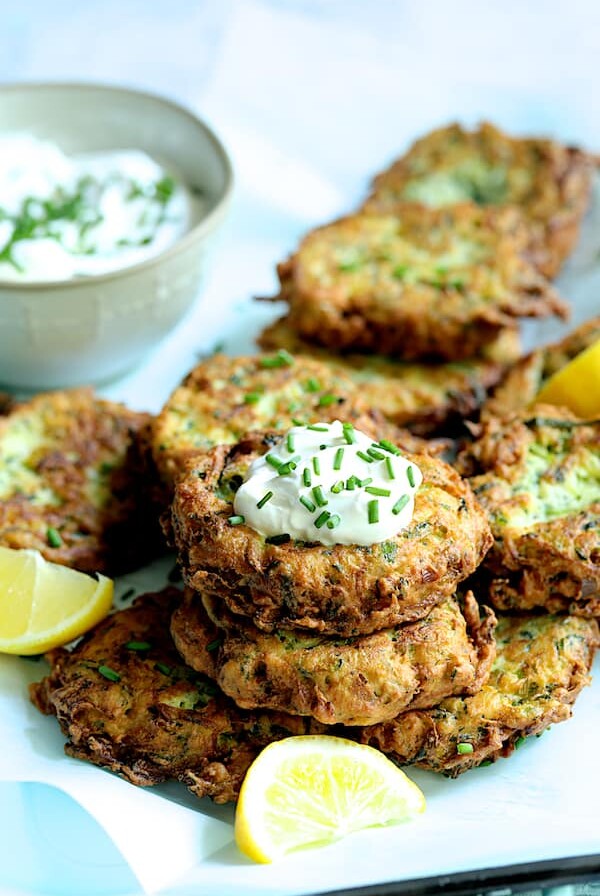 Zucchini Ricotta Fritters with yogurt chive topping garnished with lemon slices.
