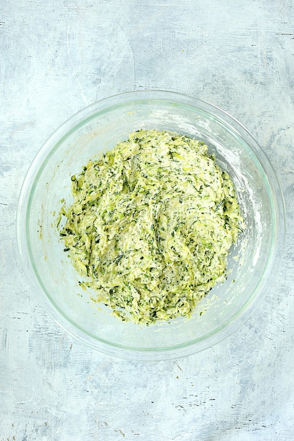 Photo of Zucchini Ricotta Fritters ingredients blended together in glass bowl.