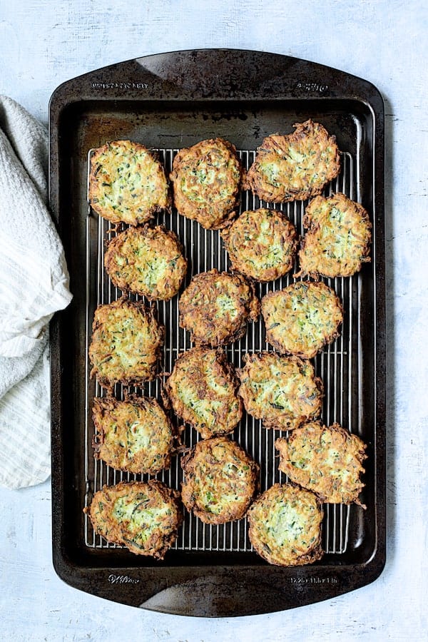 Photo of fried fritters draining on wire cooling rack set on baking sheet.