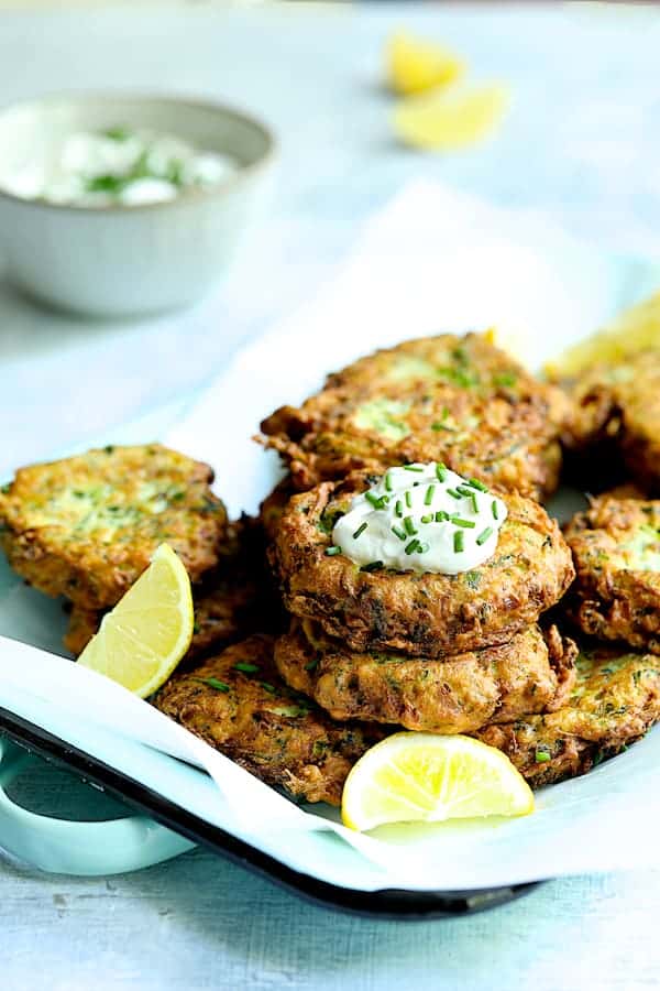 Photo of Zucchini Ricotta Fritters on parchment paper-lined serving tray garnished with lemon.