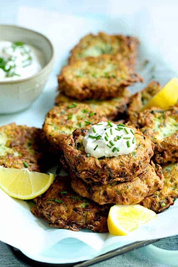 Photo of stacked Zucchini Ricotta Fritters with yogurt chive topping garnished with lemon slices.
