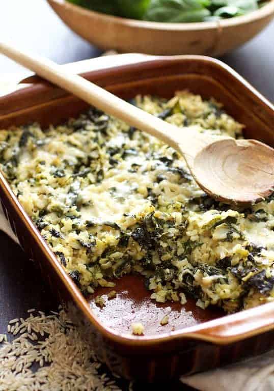 Cheesy Brown Rice and Greens Casserole in a brown rectangular baking dish with wooden spoon.