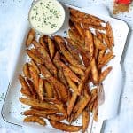 Old Bay Roasted Potato Wedges on white enameled pan with cheese sauce garnished with fresh chives and can of Old Bay.