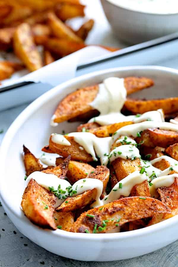 Close-up photo of Old Bay Roasted Potato Wedges with Vermont Cheddar Cheese Sauce in white bowl.