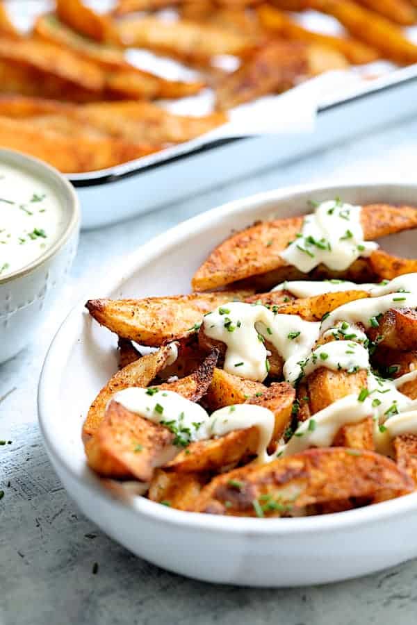 Photo of Old Bay Roasted Potato Wedges with Vermont Cheddar Cheese Sauce in white dish drizzled with cheese sauce.