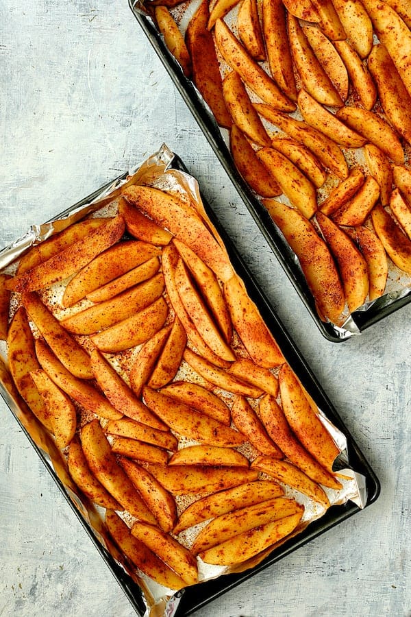 Photo of uncooked potato wedges on two sheet pans before being roasted.