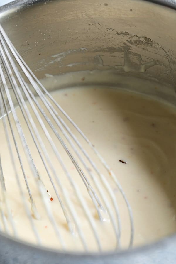 Photo of cheese sauce and whisk in saucepan.