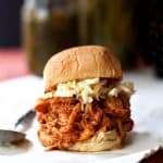 Barbecue chicken sandwich topped with coleslaw on white paper.