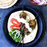 Two Turkish Ground Lamb Kebabs on pita bread on black plate.