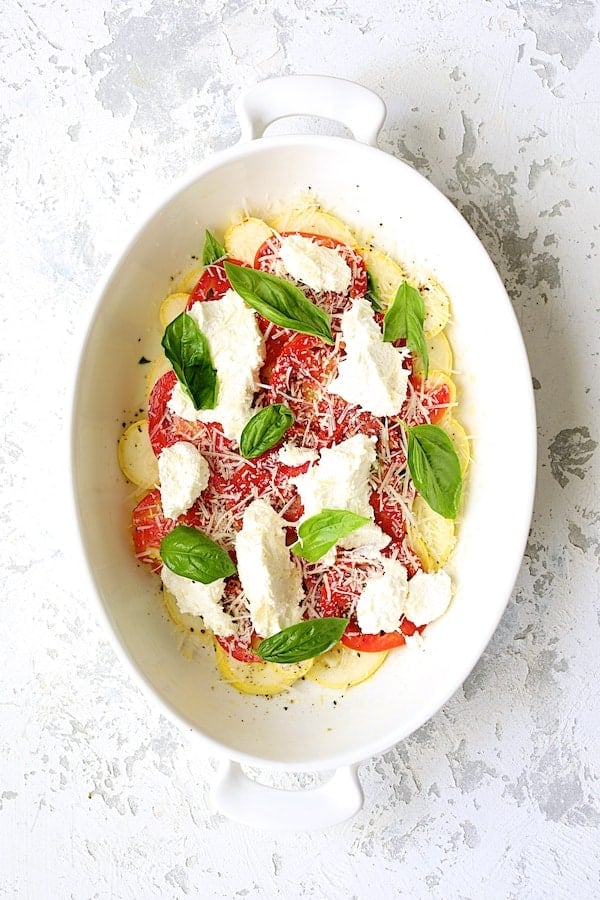 Photo after a layer of cheese and basil are added over tomato and yellow squash layers.